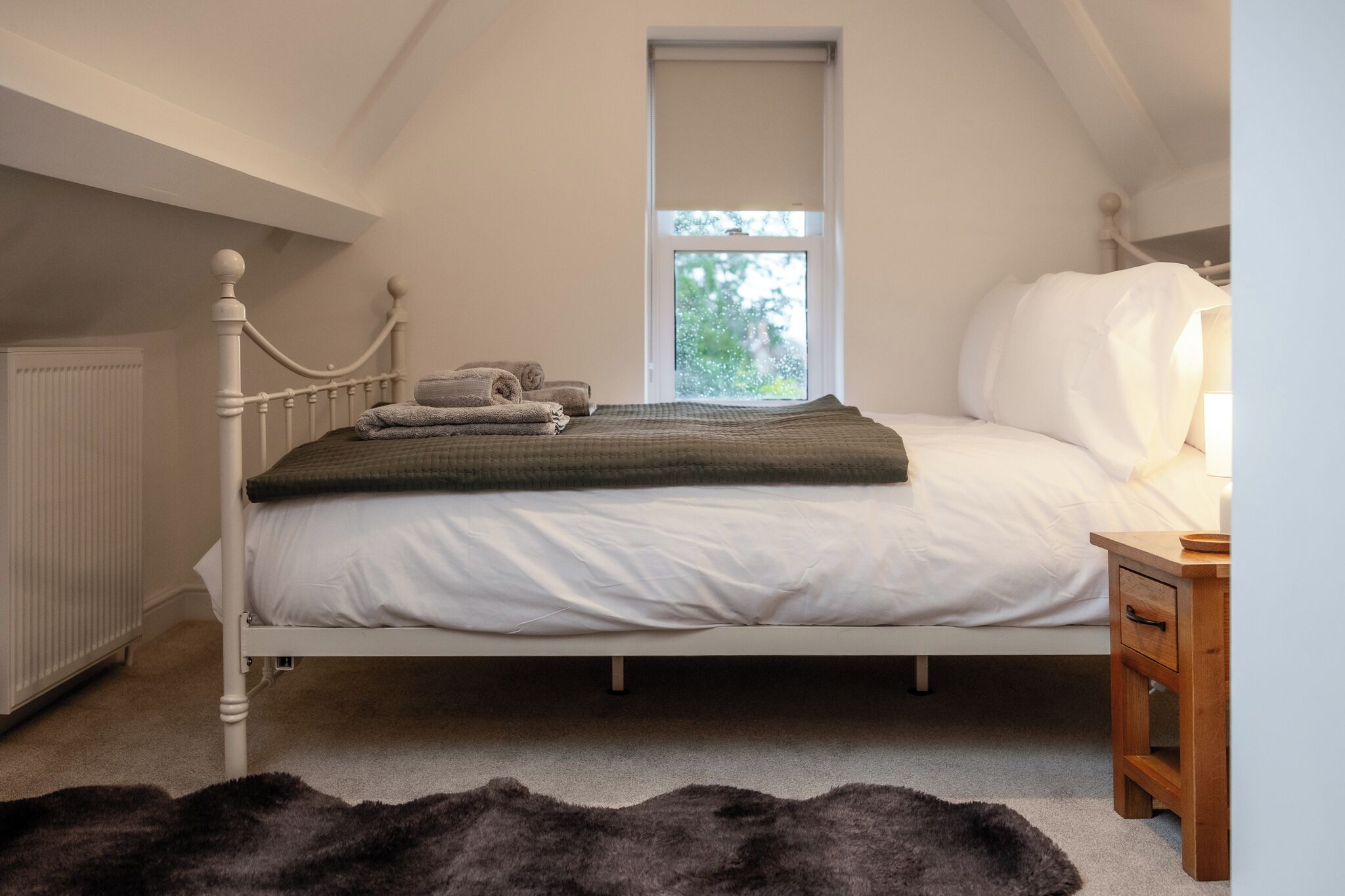 Un dormitorio con una cama individual, una ventana, un radiador y una mesita de noche de madera.