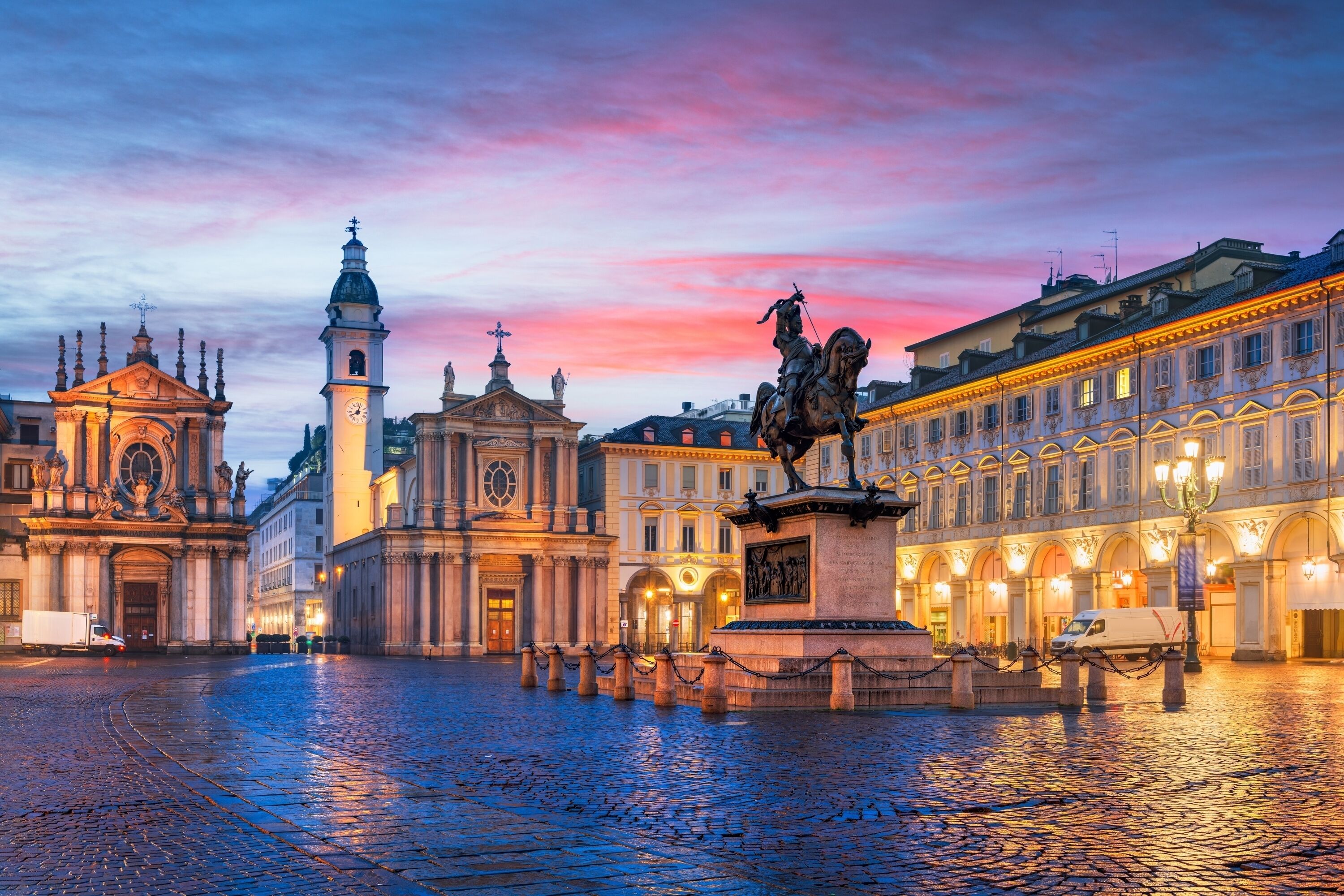 Ein historischer Platz mit einer markanten Statue, einem Glockenturm und klassischer Architektur.
