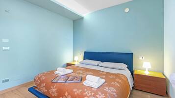 Quarto com uma cama, duas mesas de cabeceira com luminárias, cabeceira azul e colcha florida.