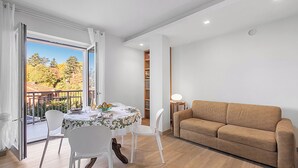 Una habitación con una mesa de comedor, sillas, un sofá, una estantería y vistas a través de un ventanal.