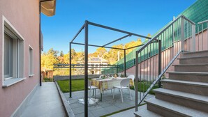 Une terrasse extérieure couverte, avec une table et des chaises, un escalier et une vue sur une maison en arrière-plan.