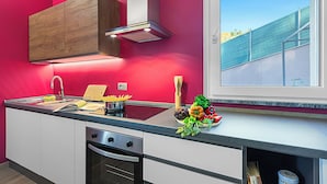 Une cuisine moderne avec un mur rouge, des appareils en acier inoxydable et une fenêtre donnant sur un immeuble.