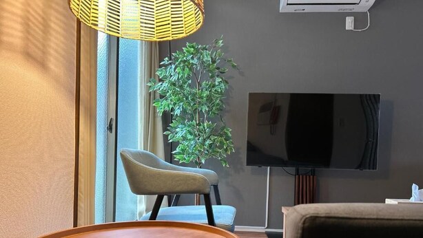 Moderni olohuone, jossa on pyöreä puinen pöytä, sohva, nojatuoli, televisio ja suuri huonekasvi.