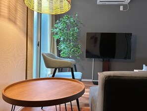 Un salon moderne avec une table ronde en bois, un canapé, un fauteuil, un téléviseur et une grande plante.