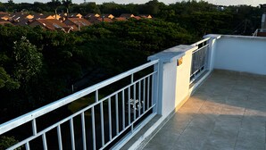 Une terrasse sur le toit, dotée d’une balustrade blanche, qui offre une vue sur un quartier résidentiel avec des maisons et des arbres.