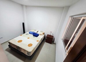 Ein kleines, ordentlich eingerichtetes Schlafzimmer mit Bett, Nachttisch und Kleiderschrank.