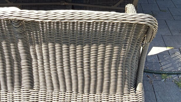Een open terras met een rieten tafel en stoelen, uitzicht op de keuken en een kleine plantenbak met beplanting.