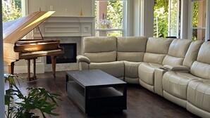 Een ruime woonkamer met een vleugelpiano, een beige modulaire bank en een marmeren vloer.
