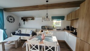 A modern kitchen with wooden cabinets, a dining area with a table and chairs, a sofa, and a clock on the wall. - Holiday Home Concordia by the Lake with Covered Terrace and Air Conditioning (Seeland)