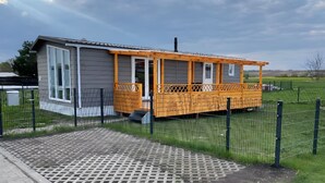 A small, single-story building with a porch and a fenced yard. - Holiday Home Concordia by the Lake with Covered Terrace and Air Conditioning (Seeland)