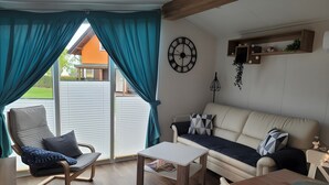 A room with a sofa, a chair, a table, and a window with curtains. - Holiday Home Concordia by the Lake with Covered Terrace and Air Conditioning (Seeland)