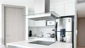 Eine moderne Küche mit einer zentralen Kochinsel, zwei Barhocker, einem Kühlschrank, einer Kaffeemaschine und einer Mikrowelle.