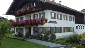 En traditionell byggnad i chaletstil med en balkong prydd med blommor, en välskött trädgård och ett trästaket i förgrunden.