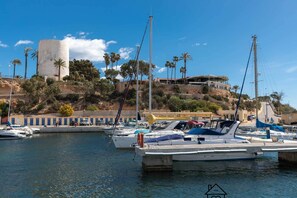A marina with boats docked, a large cylindrical structure, and a building on a hillside. - Modern apartment with jacuzzi Los Altos - Orihuela Costa (Torrevieja)
