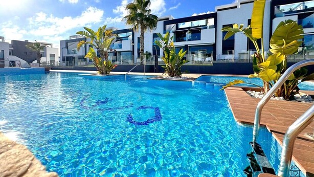 A modern hotel with a large outdoor swimming pool, surrounded by tropical plants and contemporary architecture. - Modern apartment with jacuzzi Los Altos - Orihuela Costa (Torrevieja)