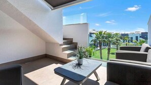 A modern balcony with a minimalist design, featuring a small table with a plant, a sofa, and a view of a residential area with palm trees and buildings. - Modern apartment with jacuzzi Los Altos - Orihuela Costa (Torrevieja)
