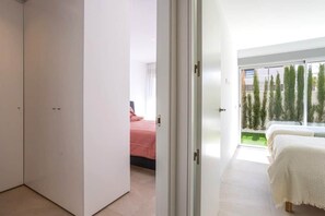 Una camera da letto moderna con un'ampia porta scorrevole in vetro che dà su un balcone con vista sugli alberi.