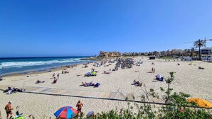 Een strand met ligbedden, parasols en mensen die ontspannen.