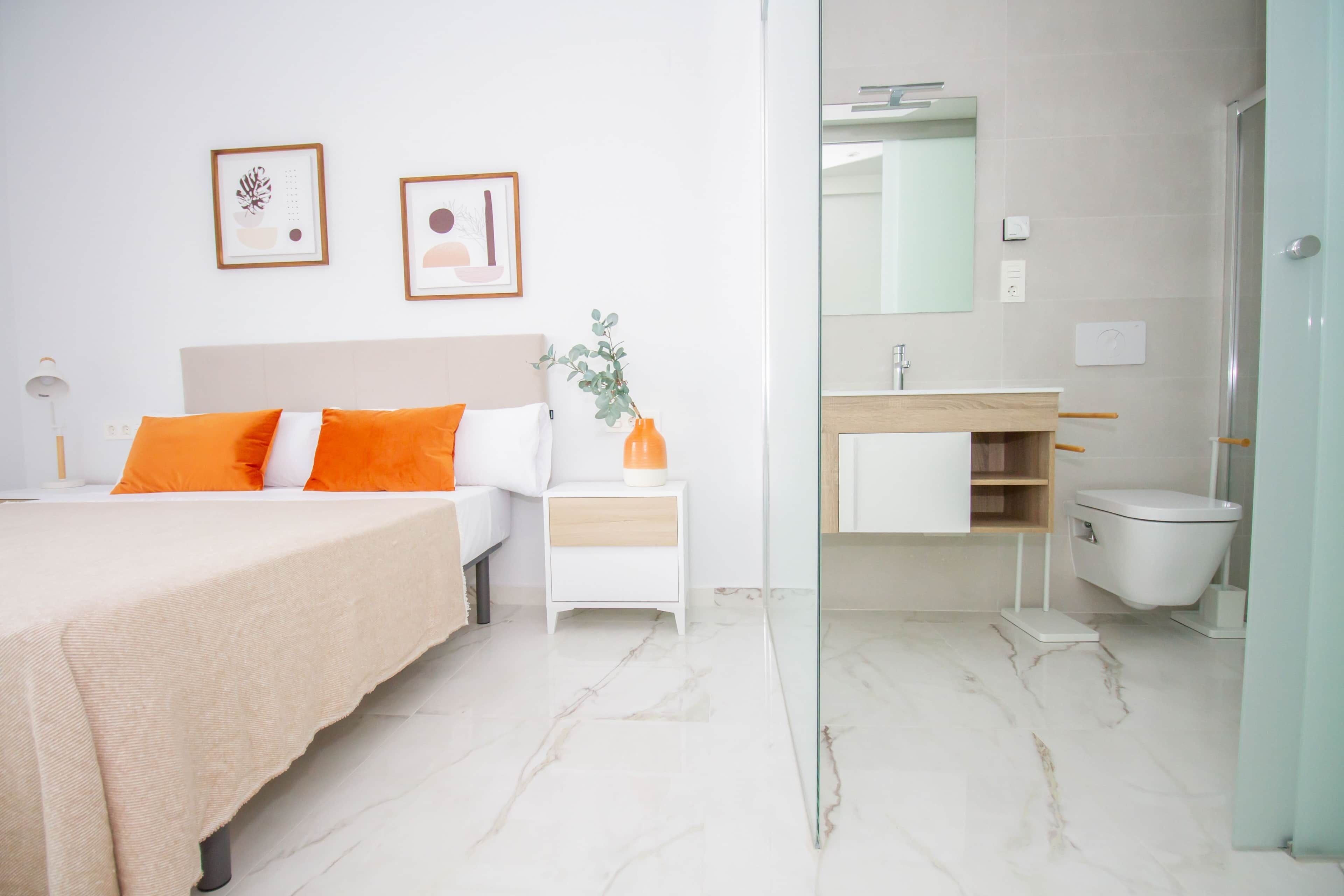 A modern hotel room with a bed, bedside table, and a bathroom with a sink, mirror, and toilet.