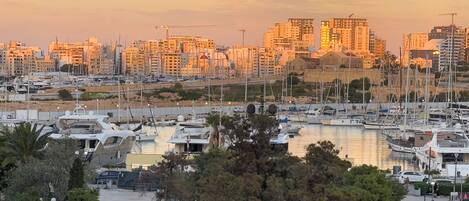 Un puerto deportivo con barcos amarrados, rodeado de edificios residenciales y grúas de construcción.