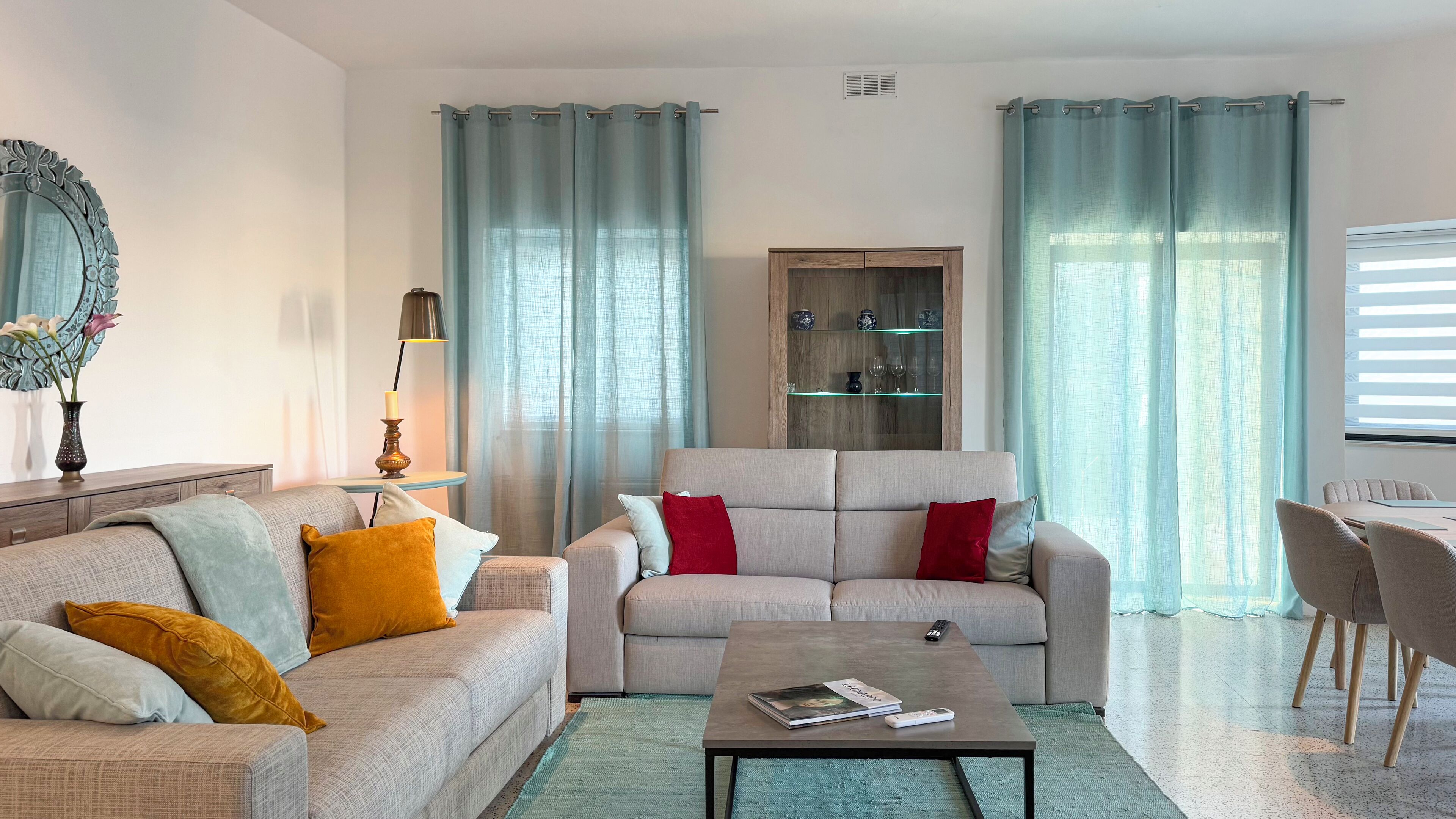 A living room with a sofa, armchair, coffee table, and a cabinet with glass shelves.