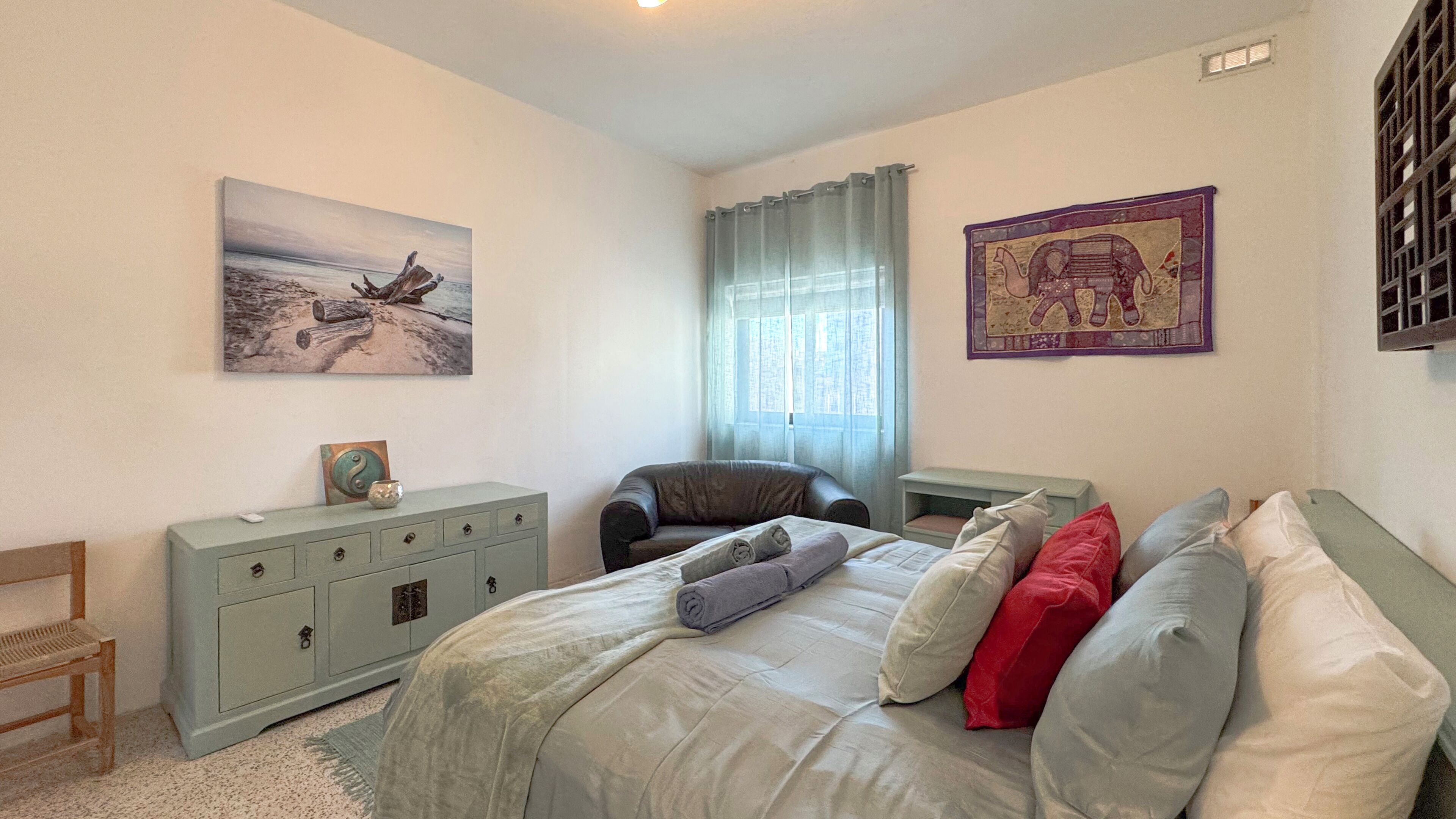 Een slaapkamer met een bed, een bureau, een stoel, een dressoir en kunstwerken aan de wanden.