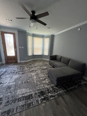 Ein Zimmer mit Deckenventilator, grauem Sofa, gemustertem Teppich und einer Tür mit dekorativem Glasfenster.