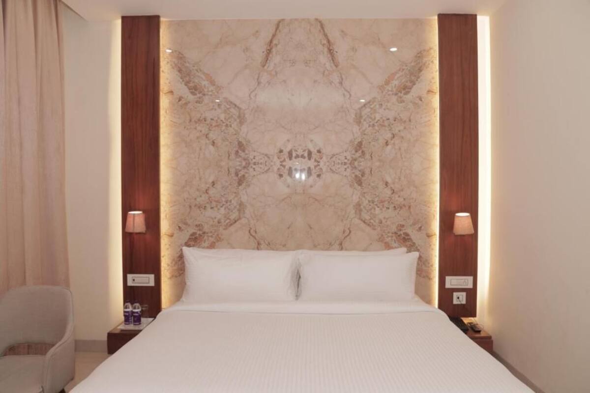 Une chambre d’hôtel avec un grand lit, une tête de lit en marbre, des lampes de chevet et un fauteuil.