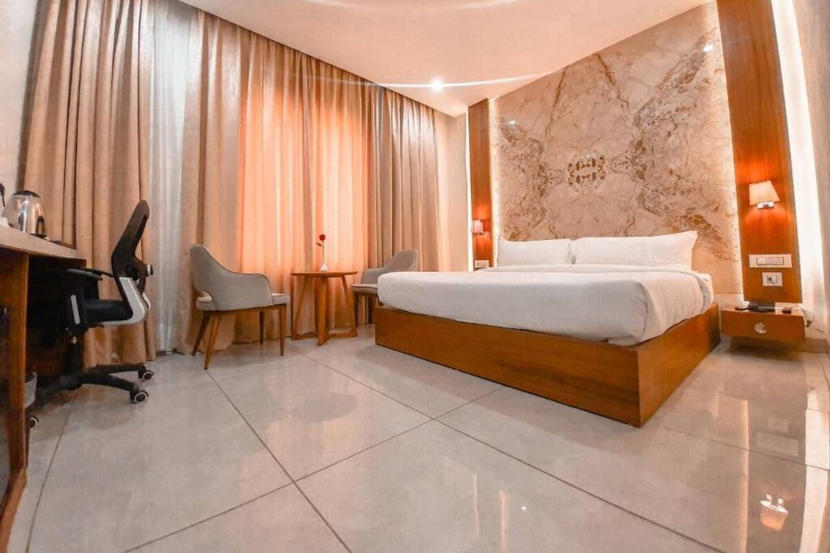 Une chambre d’hôtel moderne avec un grand lit, un bureau avec une chaise, une petite table et une lampe.