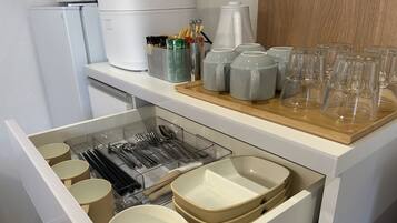 A kitchen with a drawer containing utensils and bowls, a coffee maker, and a tray with glasses and cups.