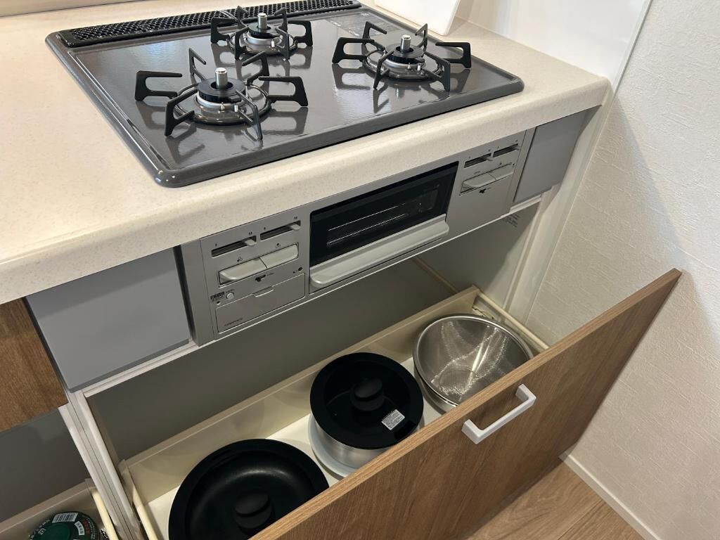Una cocina compacta con estufa a gas, horno y un cajón con utensilios de cocina.