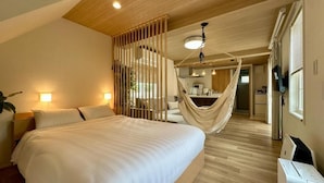 A bedroom with a large bed, a hammock, and a kitchenette in the background. - Solana Fuji Gotenba (Gotemba)