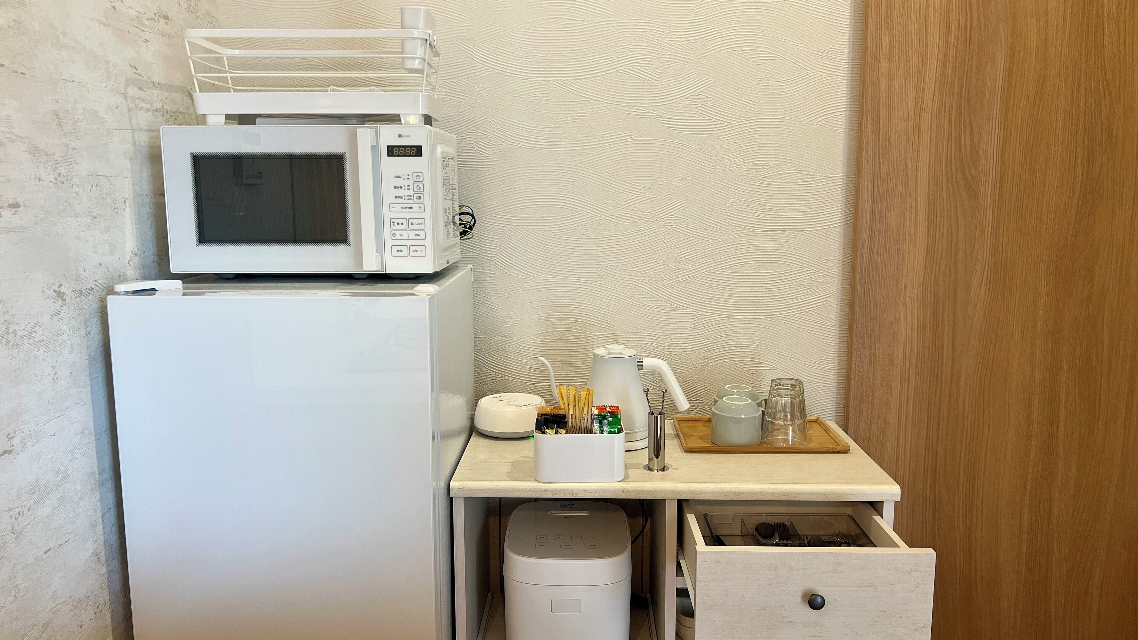 A compact kitchenette with a microwave, a small refrigerator, a coffee maker, and a tea kettle on a wooden countertop.