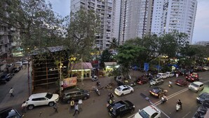 Une rue animée en milieu urbain, bordée d’immeubles résidentiels imposants, avec des voitures garées et des piétons.