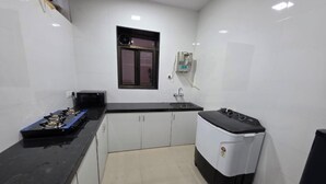 Une cuisine compacte avec des meubles blancs, un plan de travail noir, une cuisinière à gaz, un four à micro-ondes, un évier et un petit lave-linge blanc.