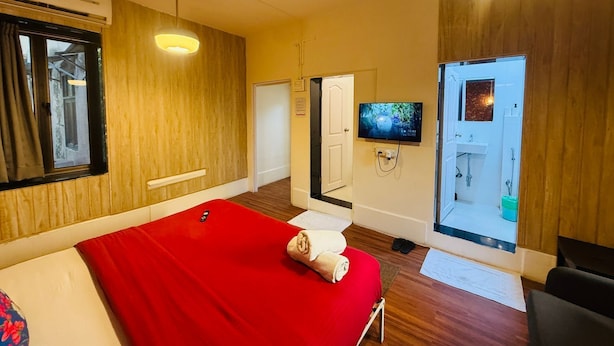 Une chambre d’hôtel avec un lit, une télévision, un ventilateur de plafond et une salle de bain visible à travers une porte ouverte.