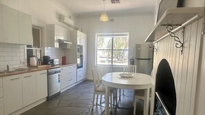 A modern kitchen with white cabinets, a dining table with chairs, a built-in oven, and a window providing natural light.