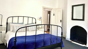 A bedroom with a bed, a white door, a black fireplace, and a wall-mounted mirror.