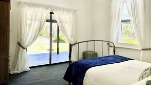 A bedroom with a bed, a window with curtains, a door, and a view of the outdoors.
