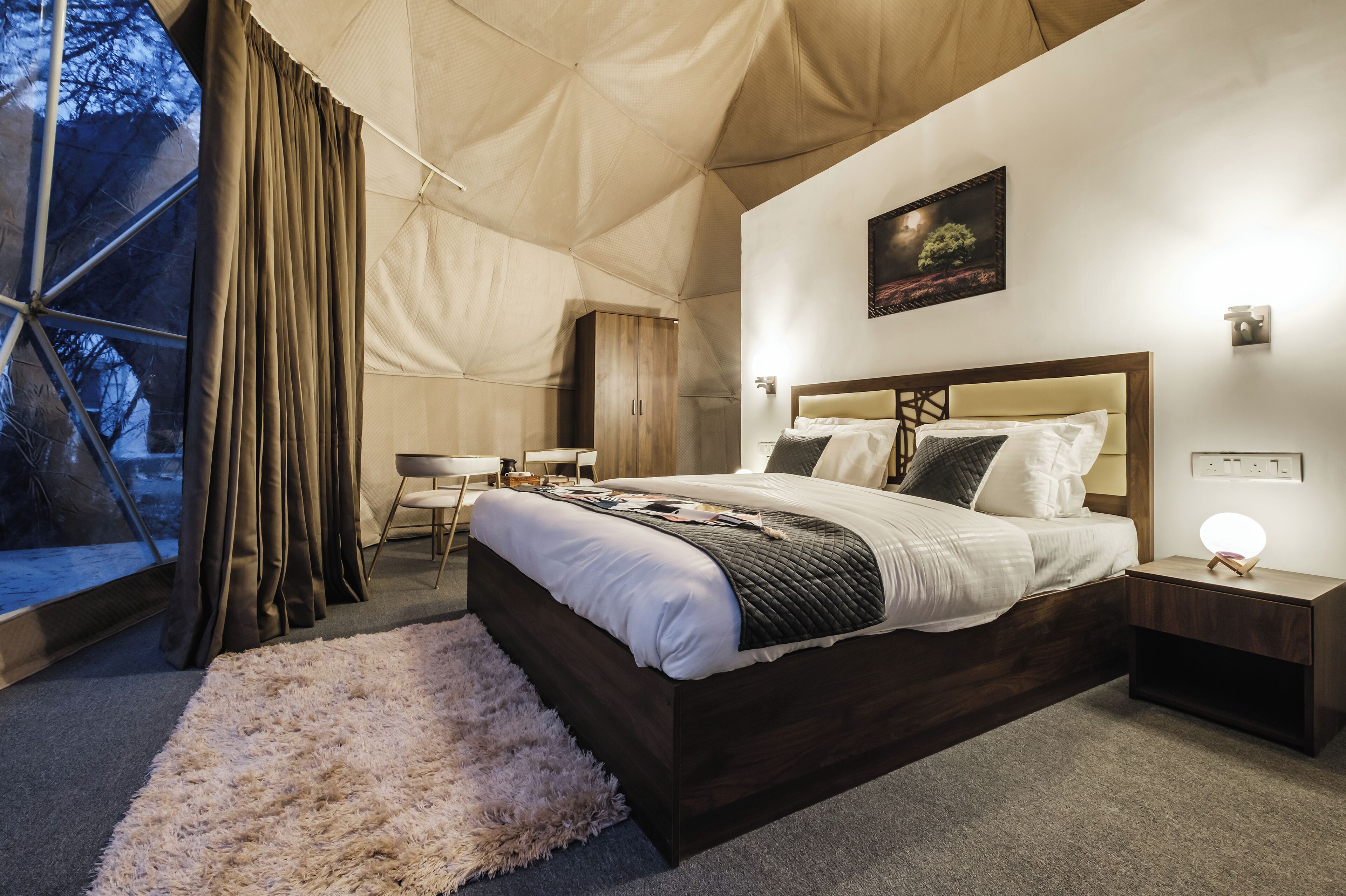 Quarto com tenda, cama, mesa de cabeceira e vista para árvores pela janela.