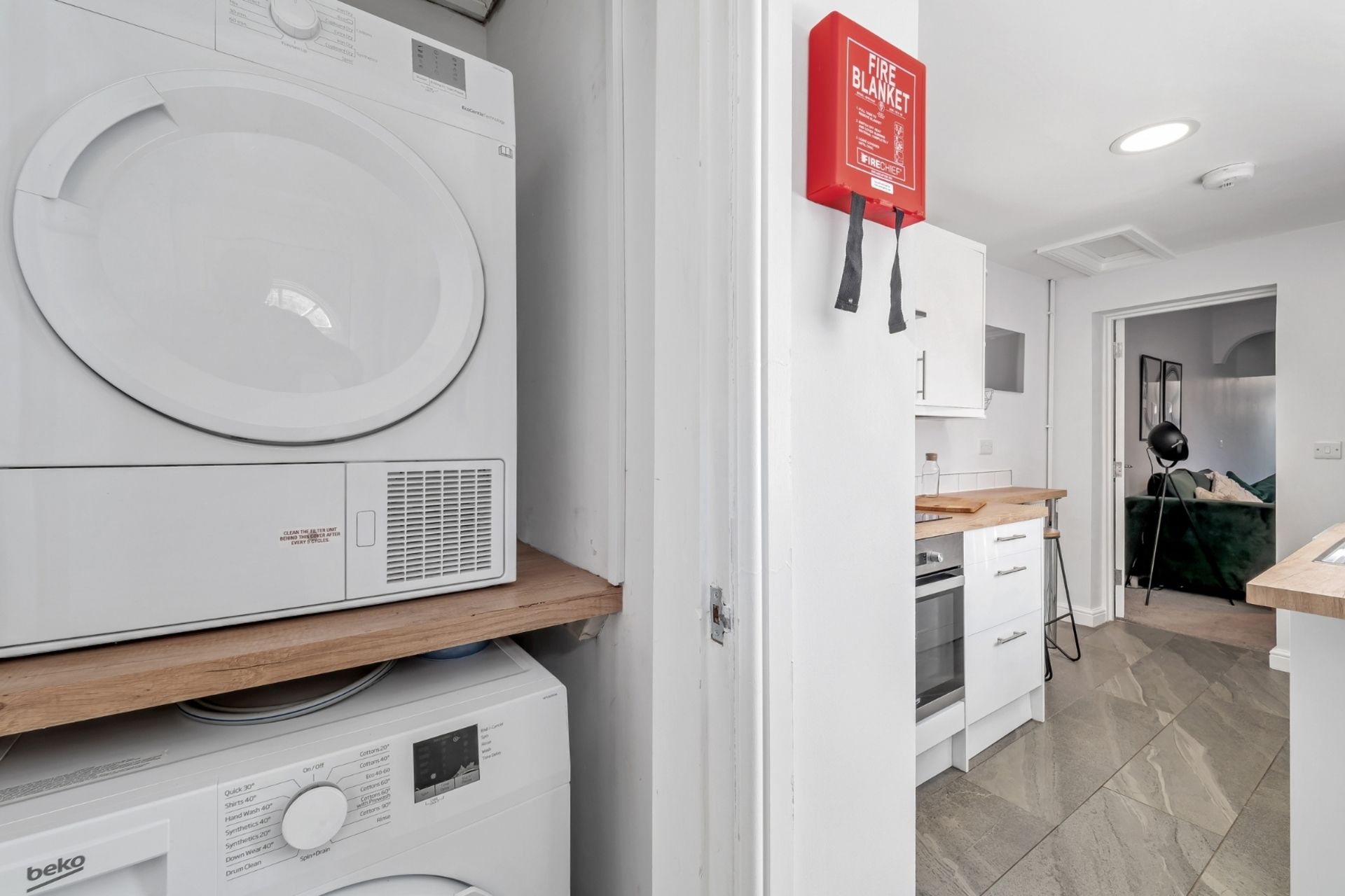 A laundry area with a washing machine, dryer, and a fire blanket mounted on the wall.