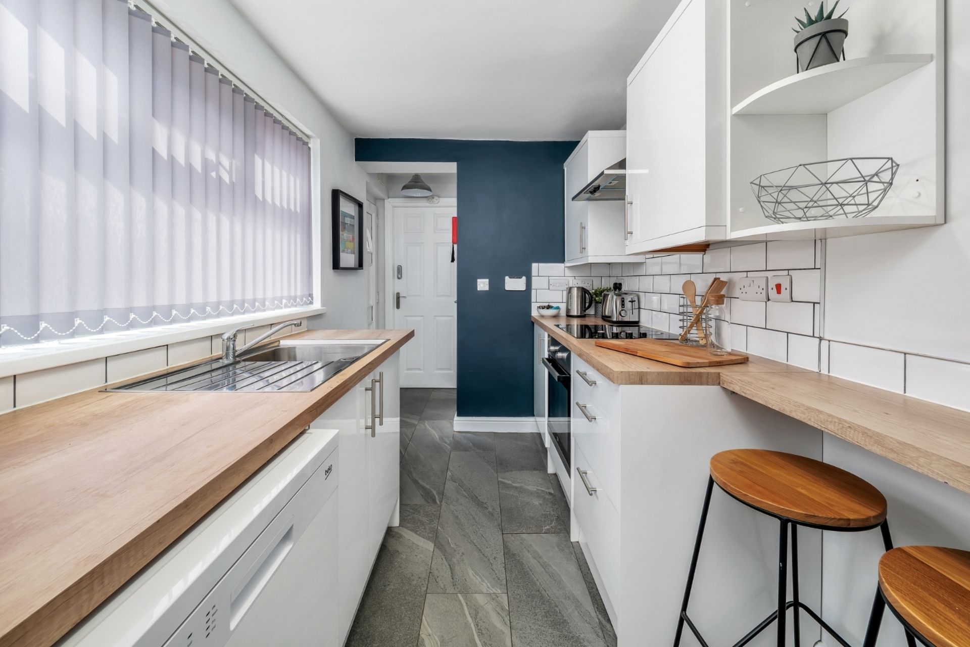 A narrow kitchen with white cabinets, a wooden countertop, and a tiled backsplash.