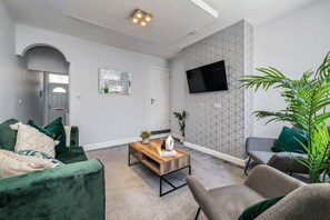 A living room with a sofa, armchair, coffee table, and a TV mounted on the wall.