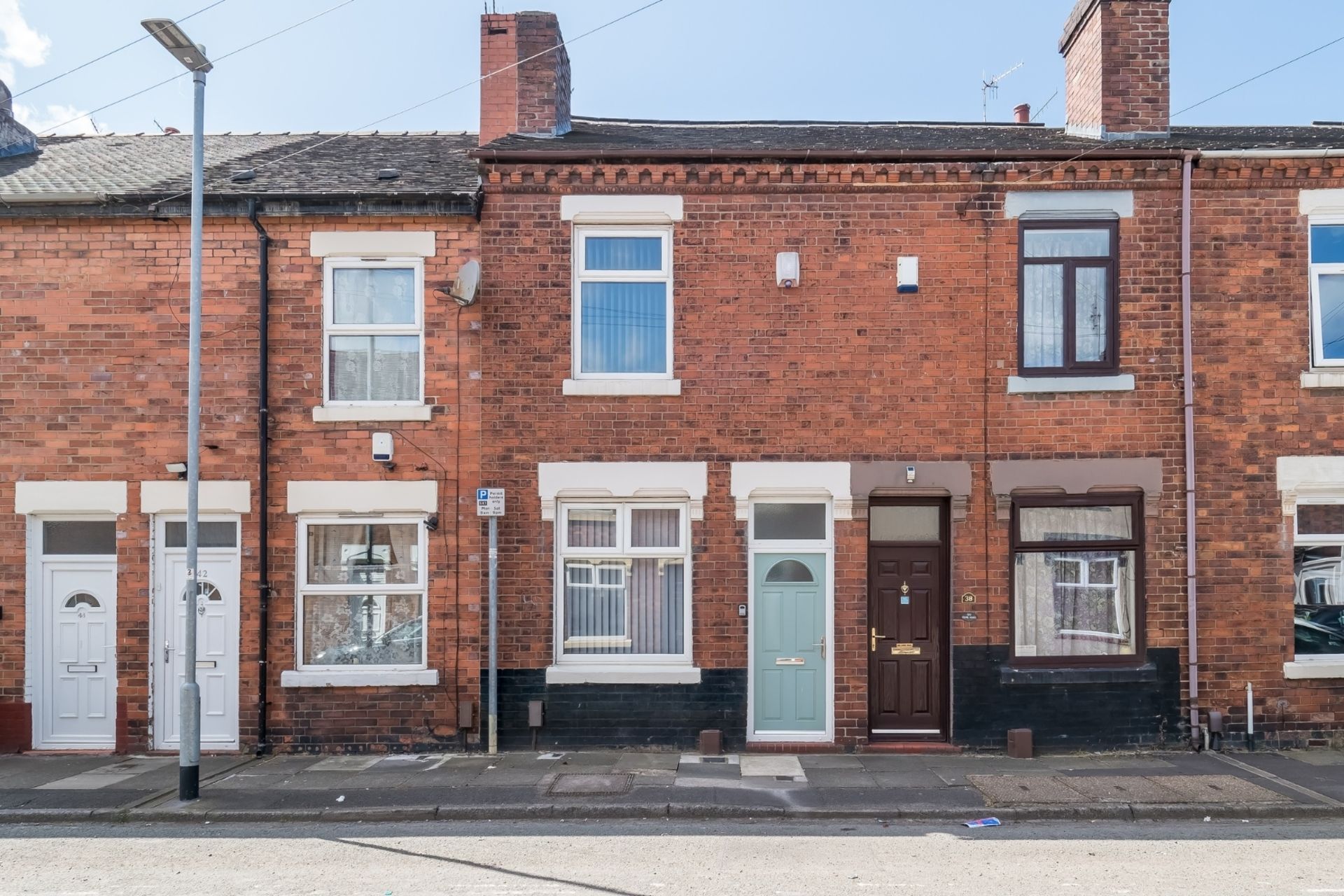 A row of red brick terraced houses with white-framed windows and doors, a clear sky, and a street lamp.