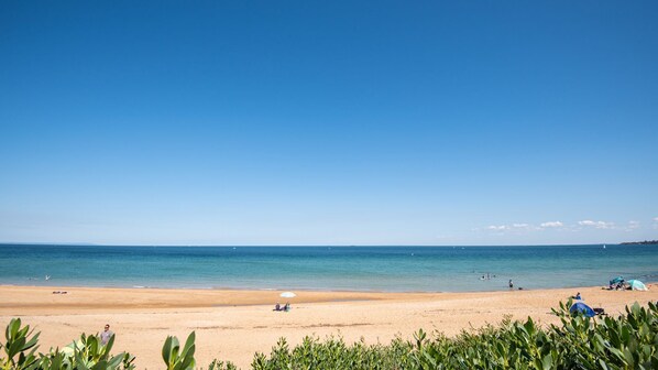 Une plage avec un ciel dégagé, une eau calme et quelques personnes et tentes.