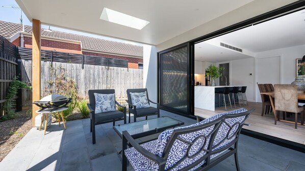 A modern patio with two chairs and a table, a sliding glass door leading to a kitchen, and a wooden fence in the background. - Miss Issy in Parkdale (Parkdale)
