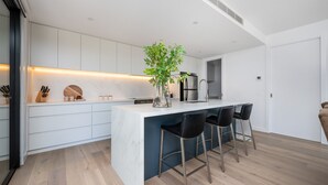 A modern kitchen with white cabinetry, a marble countertop, and a central island with bar stools. - Miss Issy in Parkdale (Parkdale)
