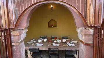 A dining table set with plates, bowls, and a vase, under an arched structure with a light fixture above.