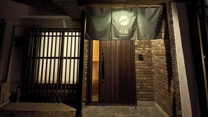 Un edificio de dos pisos con fachada oscura, una puerta de madera y un banner con caracteres japoneses.