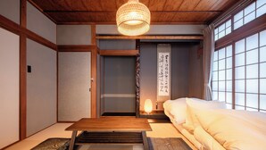 Una habitación japonesa tradicional con suelo de tatami, una mesa de madera baja, una cama con ropa blanca y un puertas correderas shoji.
